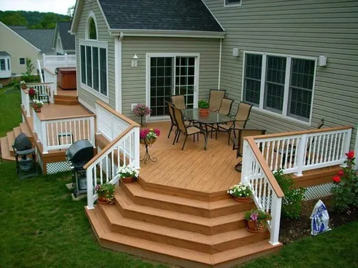 This two-level backyard deck with wide, wraparound stairs is perfect if you want clear zones for different activities without the space feeling chopped up. The upper level works beautifully as an outdoor dining area right off the house, while the lower section creates a natural transition down into the yard. Those extra-wide steps double as casual seating, which is great if you entertain often or have kids coming in and out. This style is especially well-suited to medium or larger yards and is a strong example of backyard deck ideas with stairs and backyard deck ideas two levels that feel welcoming rather than bulky. The white railing and potted plants keep it looking bright and finished without needing loads of decor.
