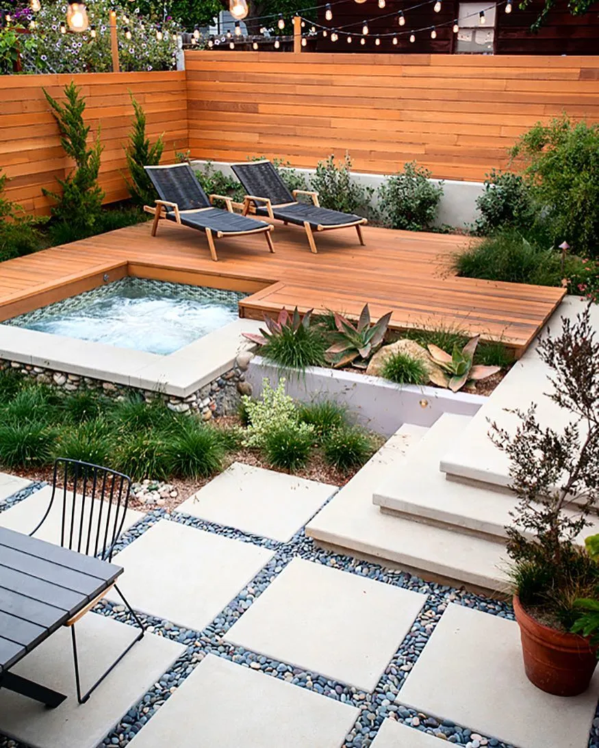 This deck landscaping idea with built-in planters, steps, and a sunken hot tub shows how smart layout choices can make even a compact backyard feel layered and intentional. The mix of decking, concrete pavers, and gravel creates clear zones for walking, relaxing, and planting, while the raised beds soften the hard edges and add greenery without taking up extra space. This setup works especially well for small to medium backyards where you want visual interest without clutter, and it’s a great example of how combining decking with landscaping features can reduce the need for lots of separate garden areas. It’s polished, low maintenance, and designed to be used — not just looked at.