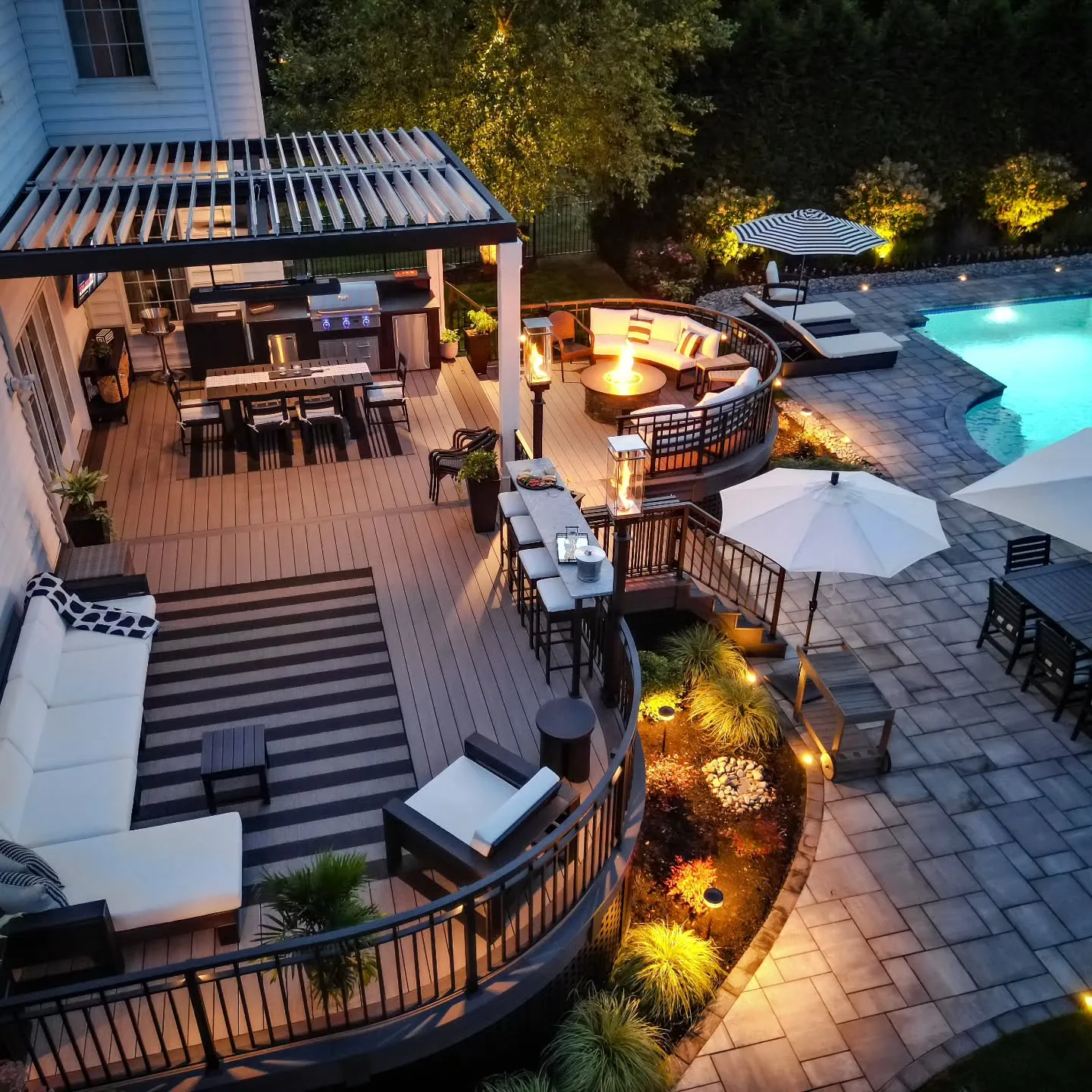 This multi-level backyard deck with a pool and built-in entertaining zones shows how decking can tie an entire outdoor space together. The curved deck edges, layered levels, and mix of seating areas make the whole backyard feel intentional rather than pieced together. You’ve got dining, lounging, and fire pit areas all flowing naturally toward the pool, which is exactly why this style works so well for backyard deck ideas with pool setups. It’s best suited to larger yards where you want different zones without hard visual breaks, and it’s a great example of backyard deck ideas two levels and backyard deck ideas with stairs that feel seamless instead of bulky. The lighting and railings do a lot of the decor work here, proving you don’t need tons of accessories when the structure itself is doing the heavy lifting.