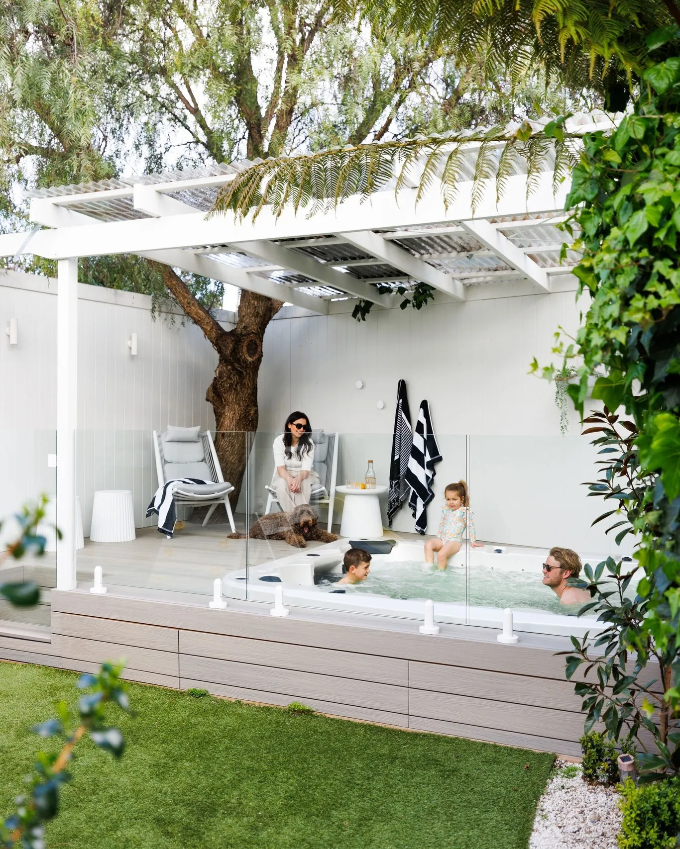 This ground-level backyard deck with a hot tub and pergola cover is a great option if you want a relaxed, modern space that works for everyday life. Keeping the deck low makes it feel open and safe, while the glass panels around the hot tub give a bit of protection without blocking the view or light. The white pergola adds shade and structure, making this a smart choice for backyard deck ideas ground level covered, especially in smaller or suburban yards. It’s also a lovely take on backyard deck ideas with hot tubs that feels calm and uncluttered rather than bulky or overbuilt — perfect if you want something stylish that still works for families and casual entertaining.