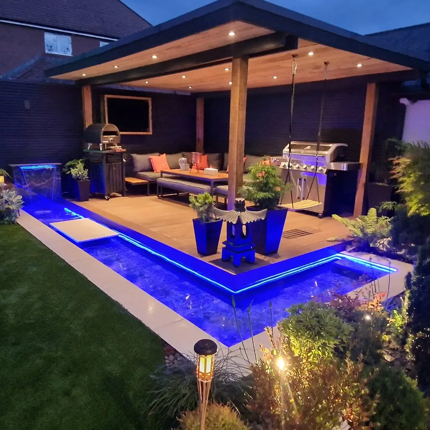 This covered backyard deck with built-in lighting and water features is designed for evening entertaining and serious relaxation. The solid roof turns the deck into a true all-weather space, while the recessed lighting and glowing water channels around the edge make it feel more like a boutique hotel than a back garden. This layout works best in medium to larger yards where you want a defined entertaining zone for lounging, grilling, and hosting without heading back inside. It’s a bold take on backyard deck ideas decor and backyard deck ideas with stairs (even low, subtle step-downs), and while it’s not a budget build, it’s brilliant inspiration if you’re planning a long-term upgrade or want to add dramatic lighting elements to a simpler deck design.
