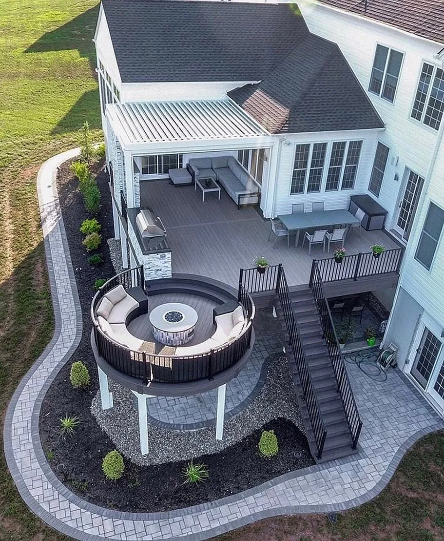 This multi-level backyard deck with a circular seating area and fire pit is designed to make the most of a sloped yard. The raised main deck connects directly to the house for dining and lounging, while the lower, round deck creates a standout conversation zone that feels separate but still connected. The curved design softens the overall look and makes the whole backyard feel custom rather than boxy. This setup is ideal for backyard deck ideas two levels and backyard deck ideas with stairs, especially if your yard isn’t flat and you want something that works with the landscape instead of fighting it. It’s definitely a higher-end build, but it’s great inspiration for anyone planning a long-term upgrade or looking to add a unique feature like a circular deck or fire pit area.