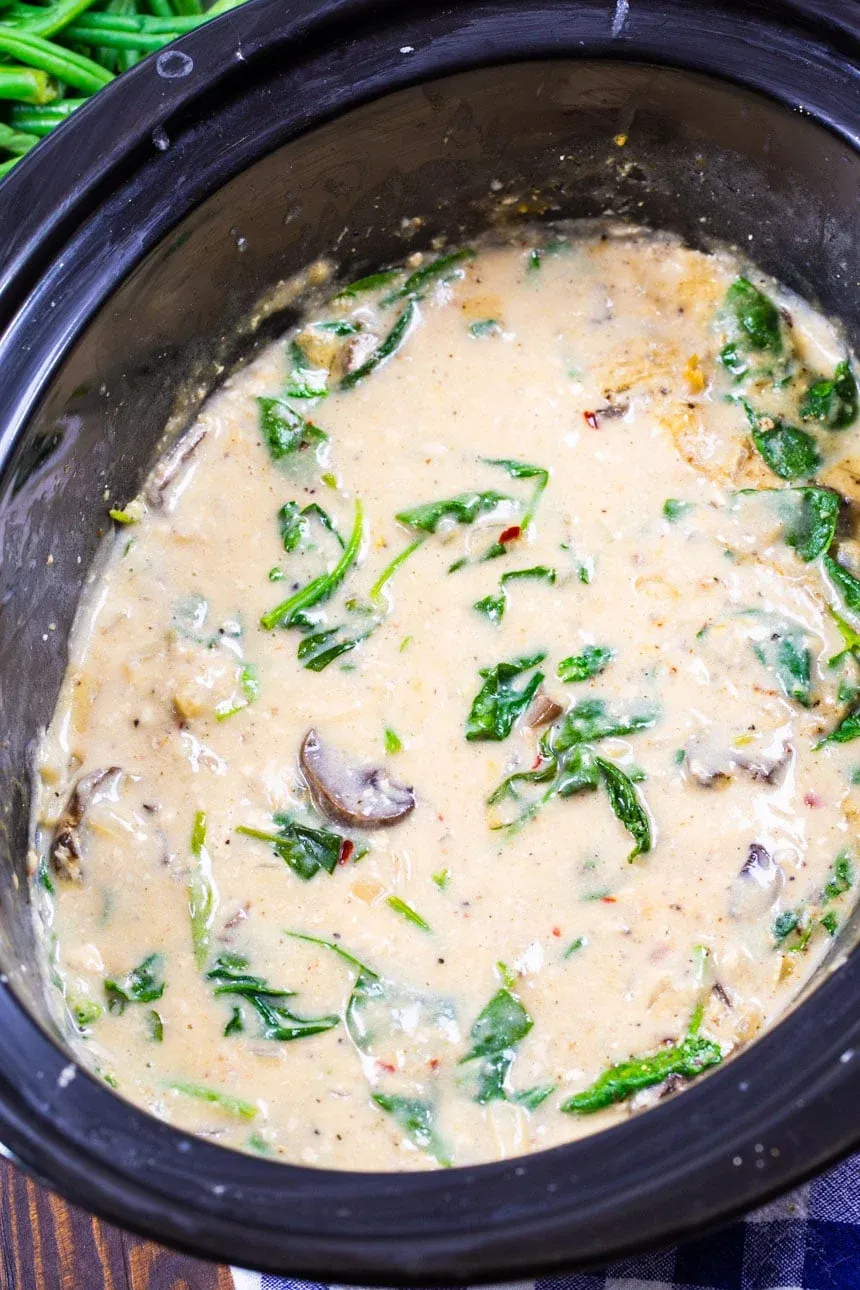 This slow cooker garlic Parmesan chicken is creamy, cozy, and full of flavor. A rich Parmesan sauce with garlic, onions, mushrooms, and spinach simmers around tender chicken to make an easy, family-friendly dinner that practically cooks itself. Perfect for busy days when you want something comforting waiting at dinnertime.