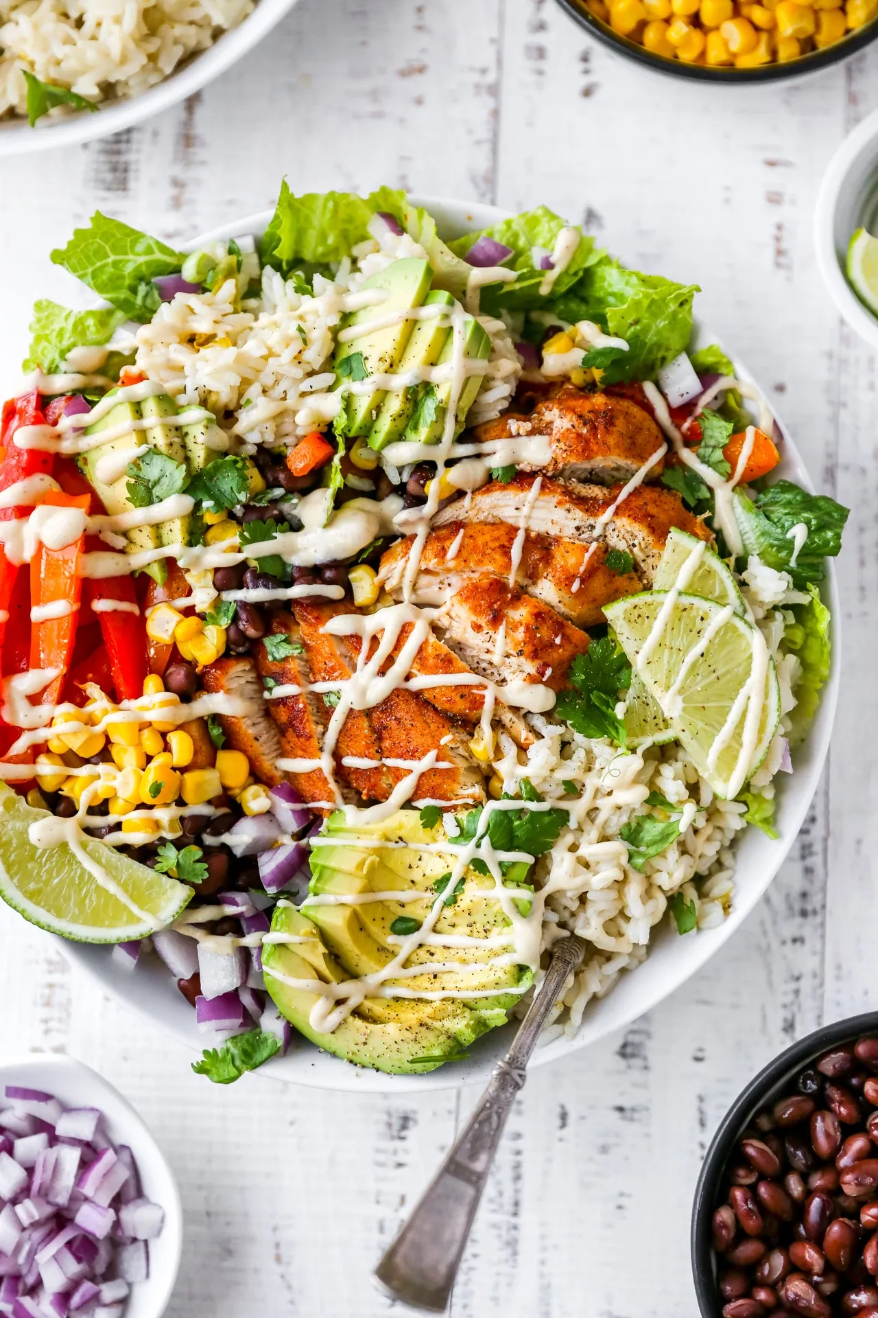 These chicken burrito bowls are piled high with fajita-seasoned chicken, bell peppers, black beans, sweet corn, red onion, cilantro-lime rice, crisp romaine, and creamy avocado, all drizzled with a bright cilantro-lime dressing. It’s one of those burrito bowl recipes that works just as well for a quick family dinner as it does for healthy lunches for work. Super colorful, super filling, and easy to tweak based on what you have in the fridge, this is the kind of healthy burrito bowl you’ll find yourself making on repeat.